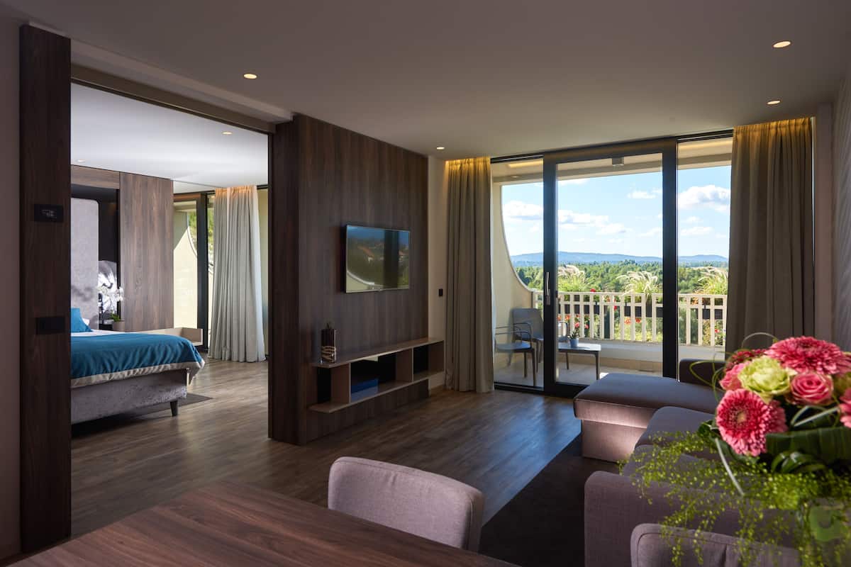 Habitación de hotel moderna con una cama grande, televisión, balcón con vistas y zona de comedor.