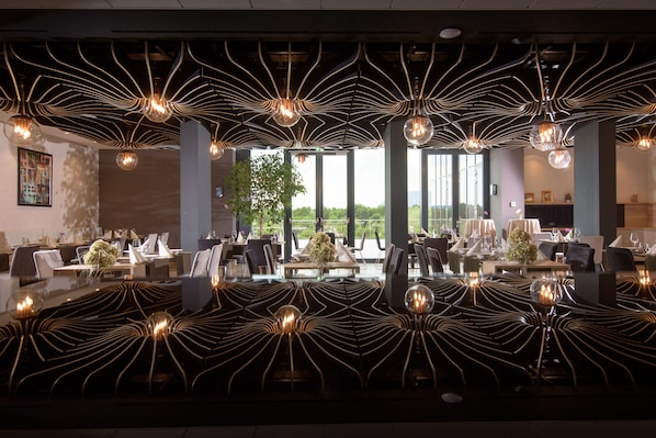 A modern restaurant with a unique ceiling design, large windows, and a view of the outdoors.
