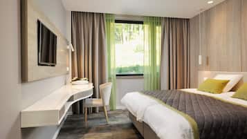 Una habitación de hotel moderna con una cama, un escritorio con silla, un televisor en la pared y una ventana con cortinas.