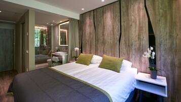 Quarto moderno com uma cama grande, uma mesa de cabeceira com uma planta e vista para um banheiro.