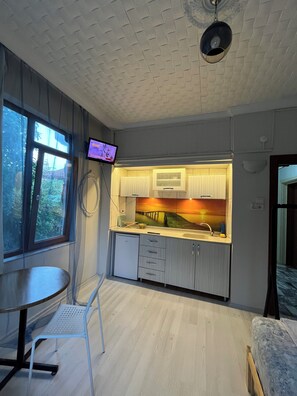 Una habitación compacta con kitchenette, un pequeño comedor y un televisor montado en la pared.