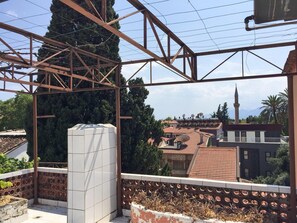 Un balcón con estructura metálica, una maceta blanca y vistas a edificios, una mezquita y montañas al fondo.