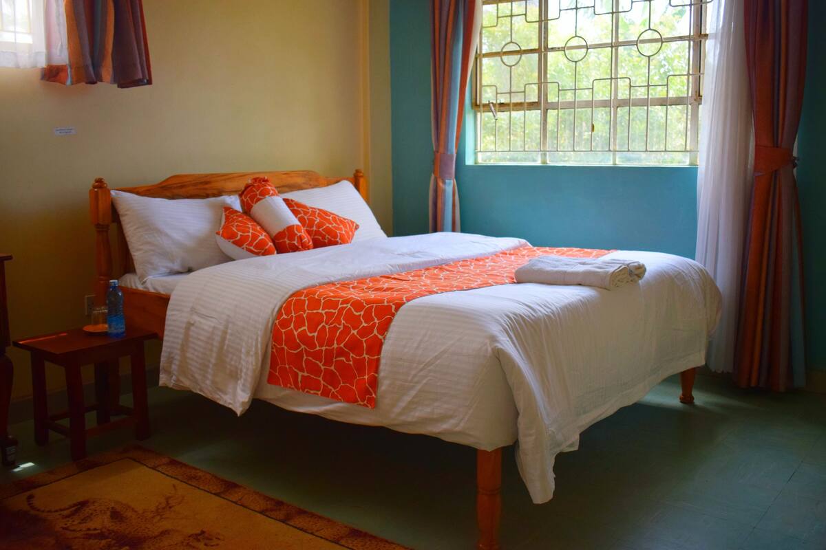 Una cama bien hecha con ropa de cama blanca y naranja, un cabecero de madera y una ventana con barrotes.