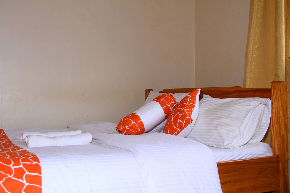 Una cama bien tendida con ropa blanca y almohadas estampadas en naranja, un cabecero de madera y una colcha con estampado rojo y blanco.