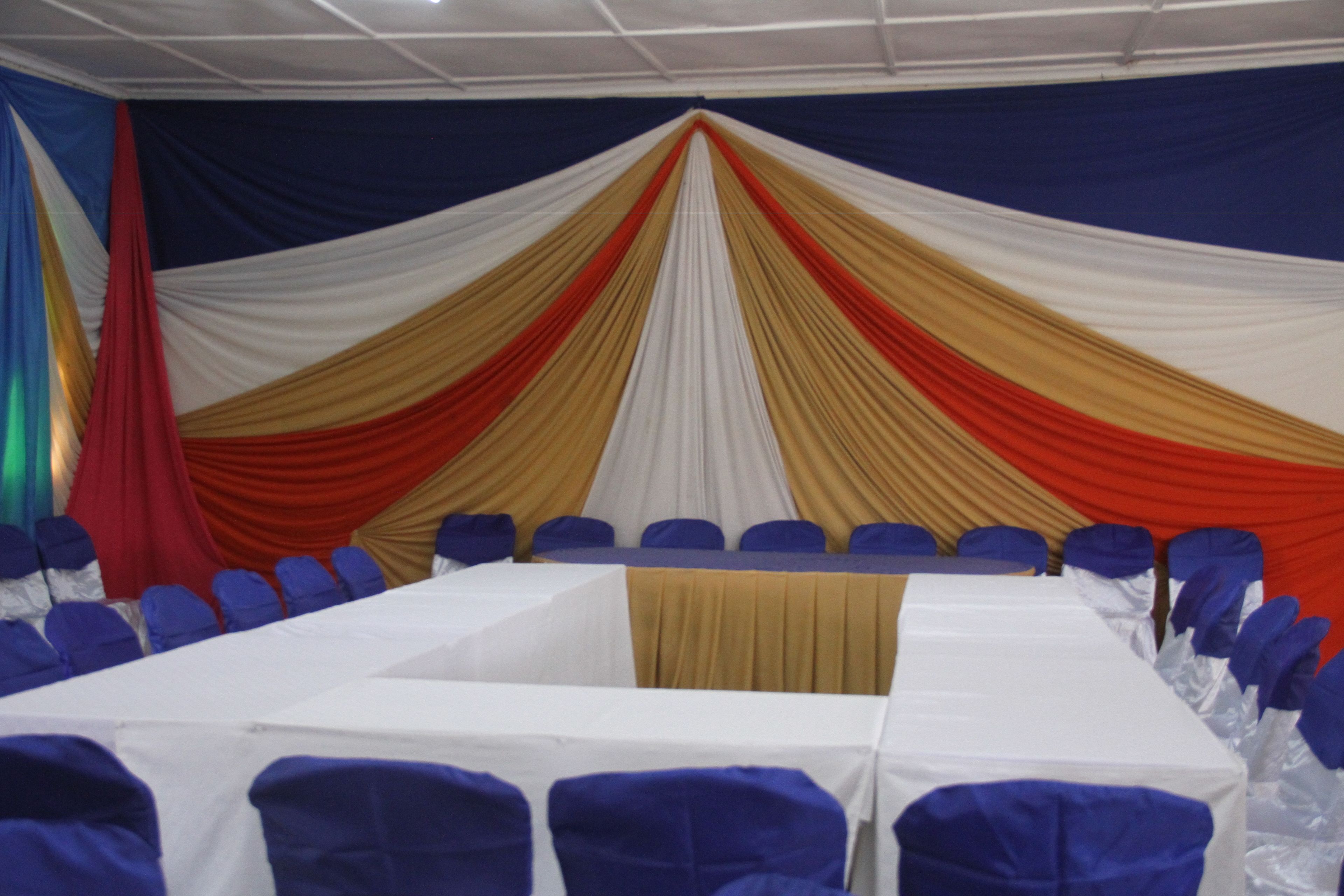 A conference room with a long table, blue chairs, and draped curtains in white, red, and gold.