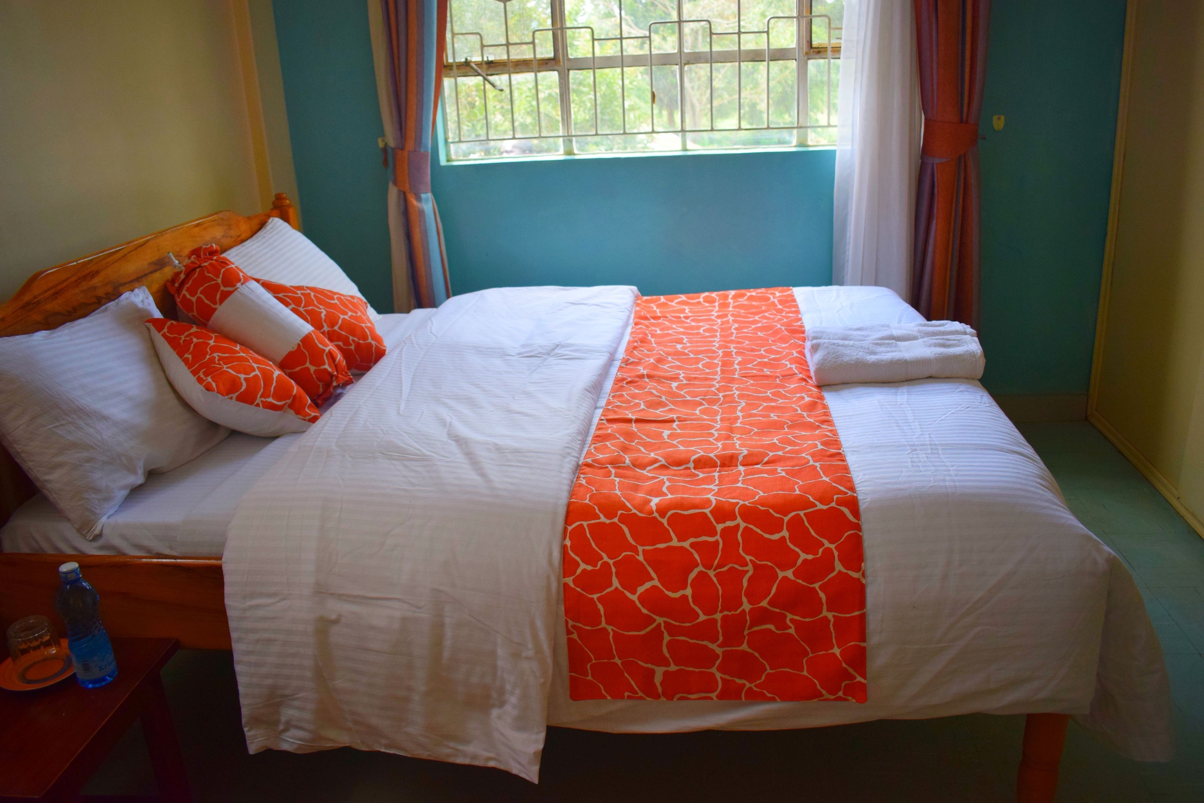 Una cama con ropa de cama blanca y naranja, un cabecero de madera y una ventana con cortinas.