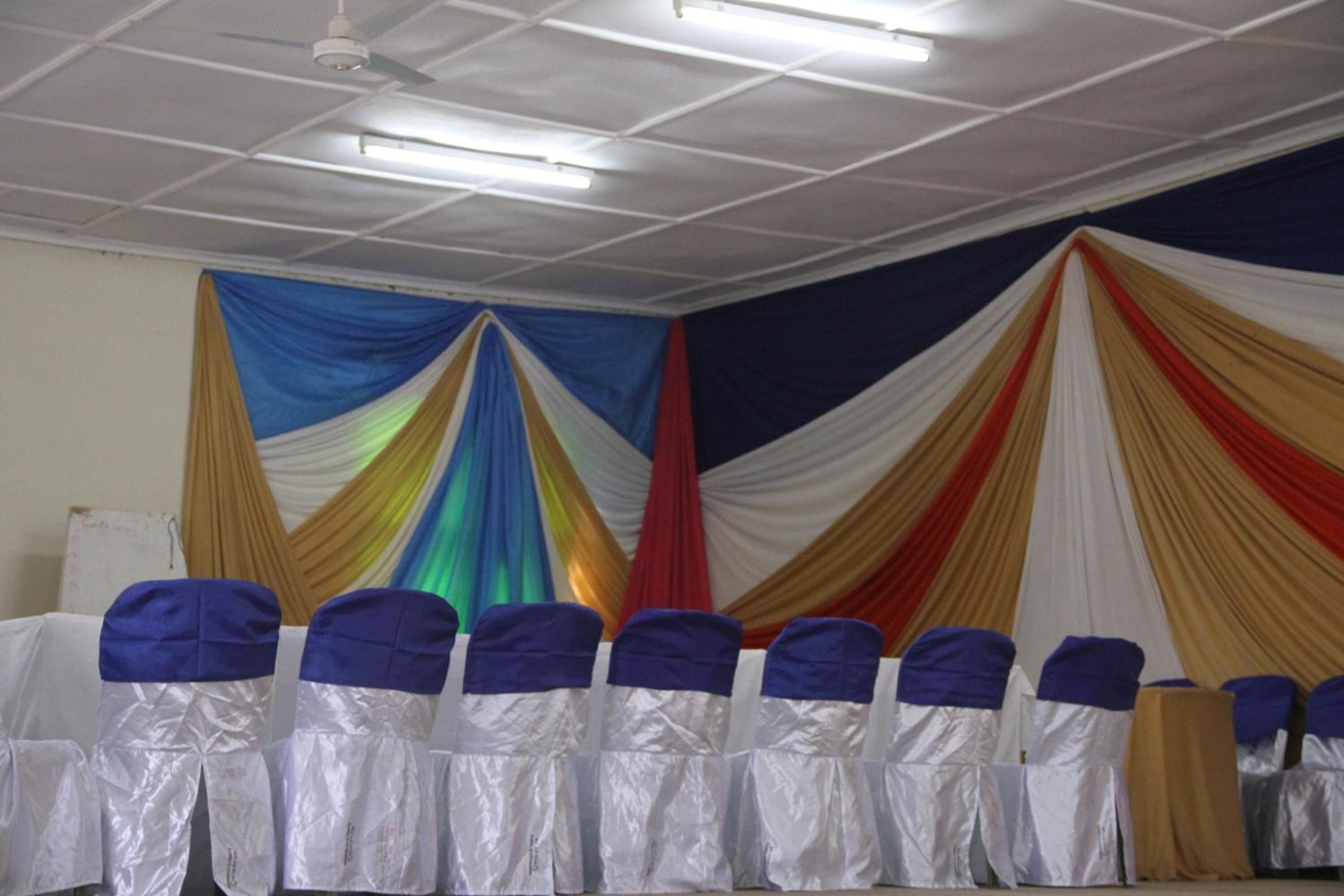 A room with white ceiling panels, a white table, and chairs with blue and white covers.