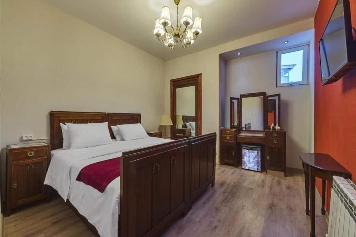 A hotel room with a large bed, wooden furniture, a chandelier, a television, and a mirror.