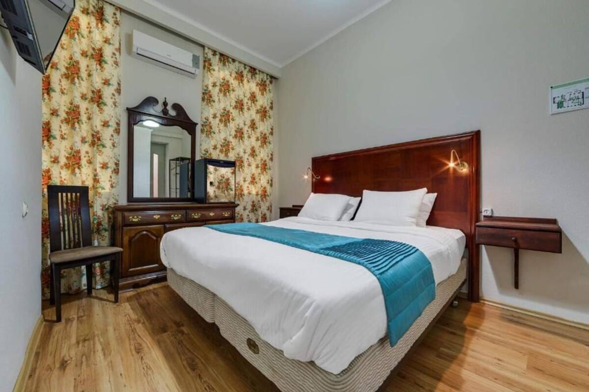 A bedroom with a wooden bed, a nightstand, a dresser, a mirror, and floral wallpaper.