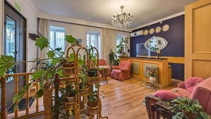 Una sala de estar acogedora con suelo de madera, una araña, una chimenea y una zona de estar con un sofá rosa y sillones.