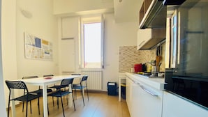 A modern kitchen with white cabinets, a dining table with chairs, a window, and a built-in oven. - Liola Home (Palermo)