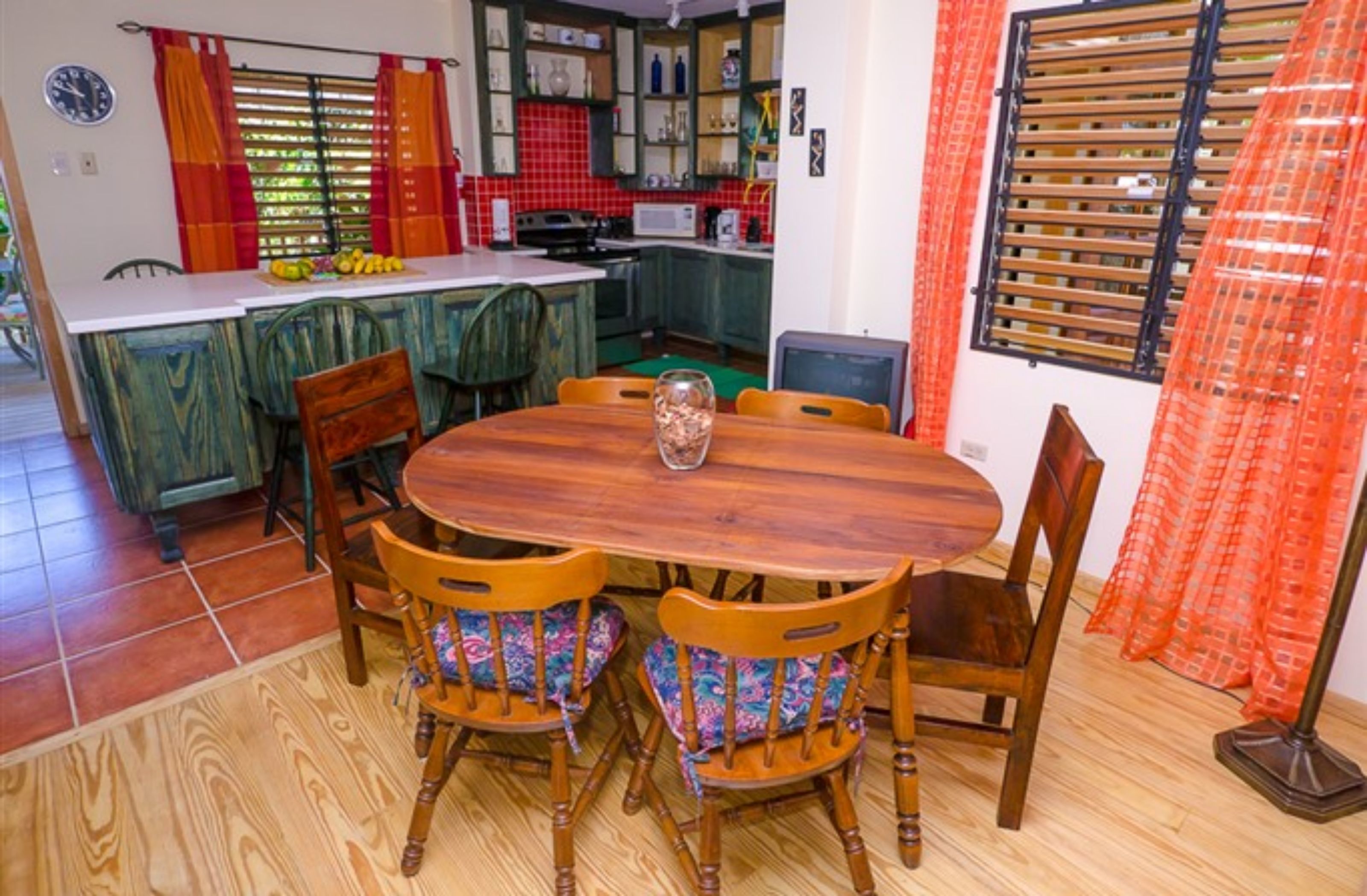 Un coin repas avec une table et des chaises en bois, une cuisine à l’arrière-plan et une fenêtre avec des rideaux.