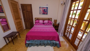 A bedroom with a wooden bed, a bench, a wooden door, and a window with curtains.