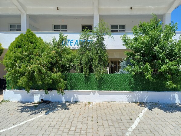 Un edificio con un letrero que dice “HOTEL ACADEMY” y un área pavimentada con árboles y arbustos.