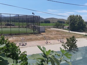 A sports field with exercise equipment, a fenced area, and a view of distant hills. - Elite Apart Pansiyon (Gökçeada)