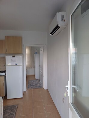 Cocina compacta con refrigerador, estufa y unidad de aire acondicionado. Un pasillo conduce a una puerta con cerradura.