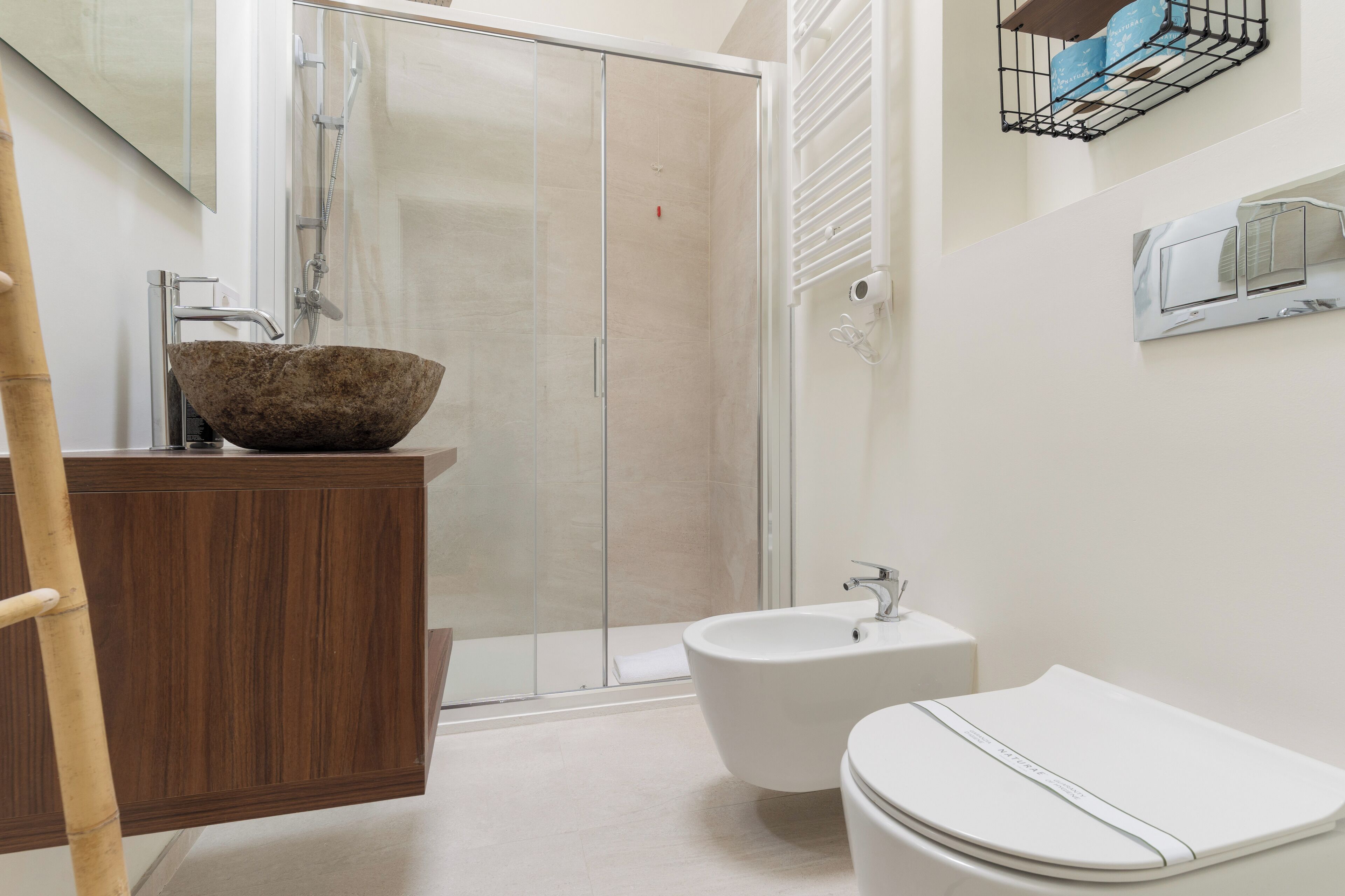 A bathroom with a wooden vanity, a white sink, a bidet, and a glass shower enclosure.