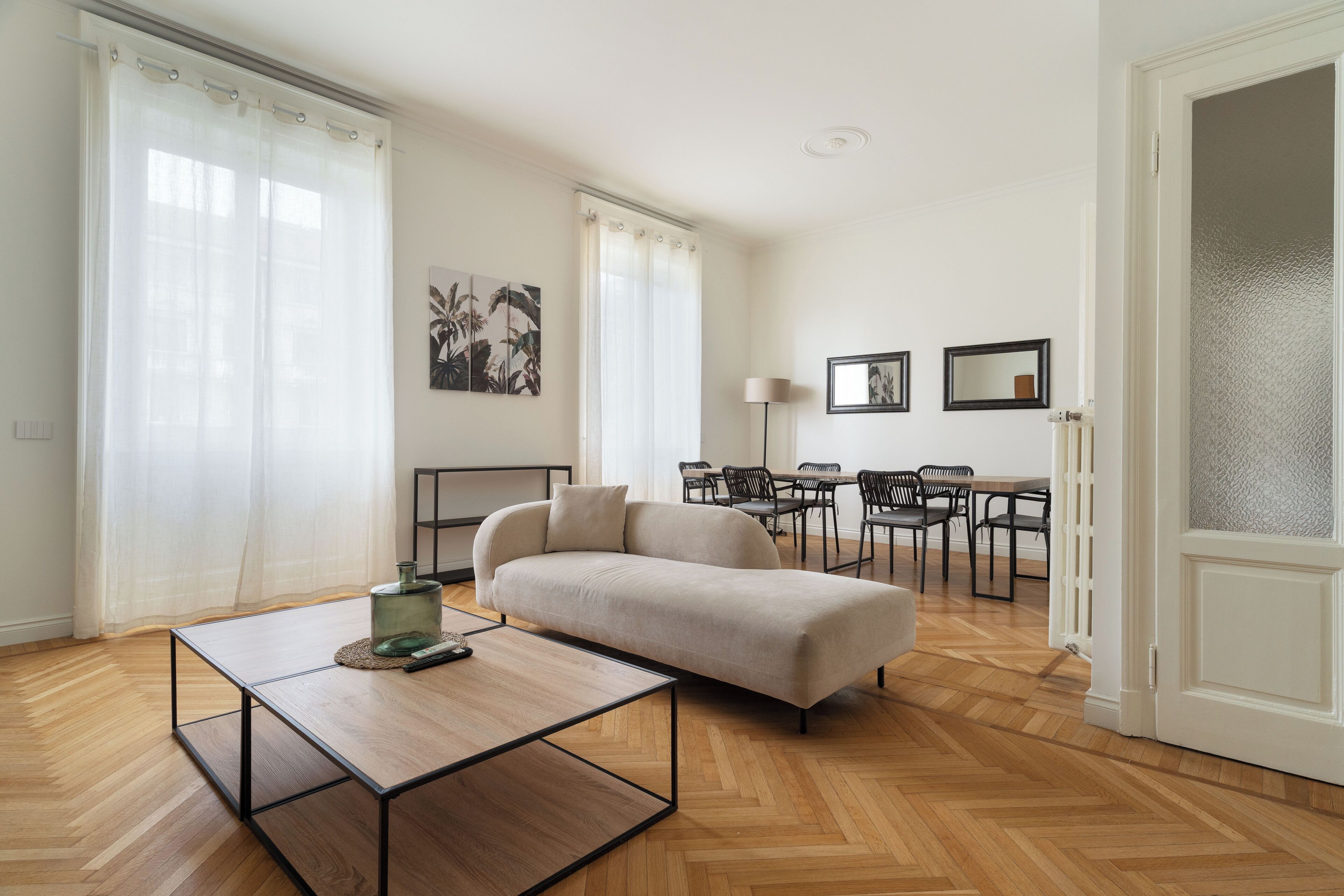 A modern living room with a sofa, a coffee table, and a dining area with chairs and a table.