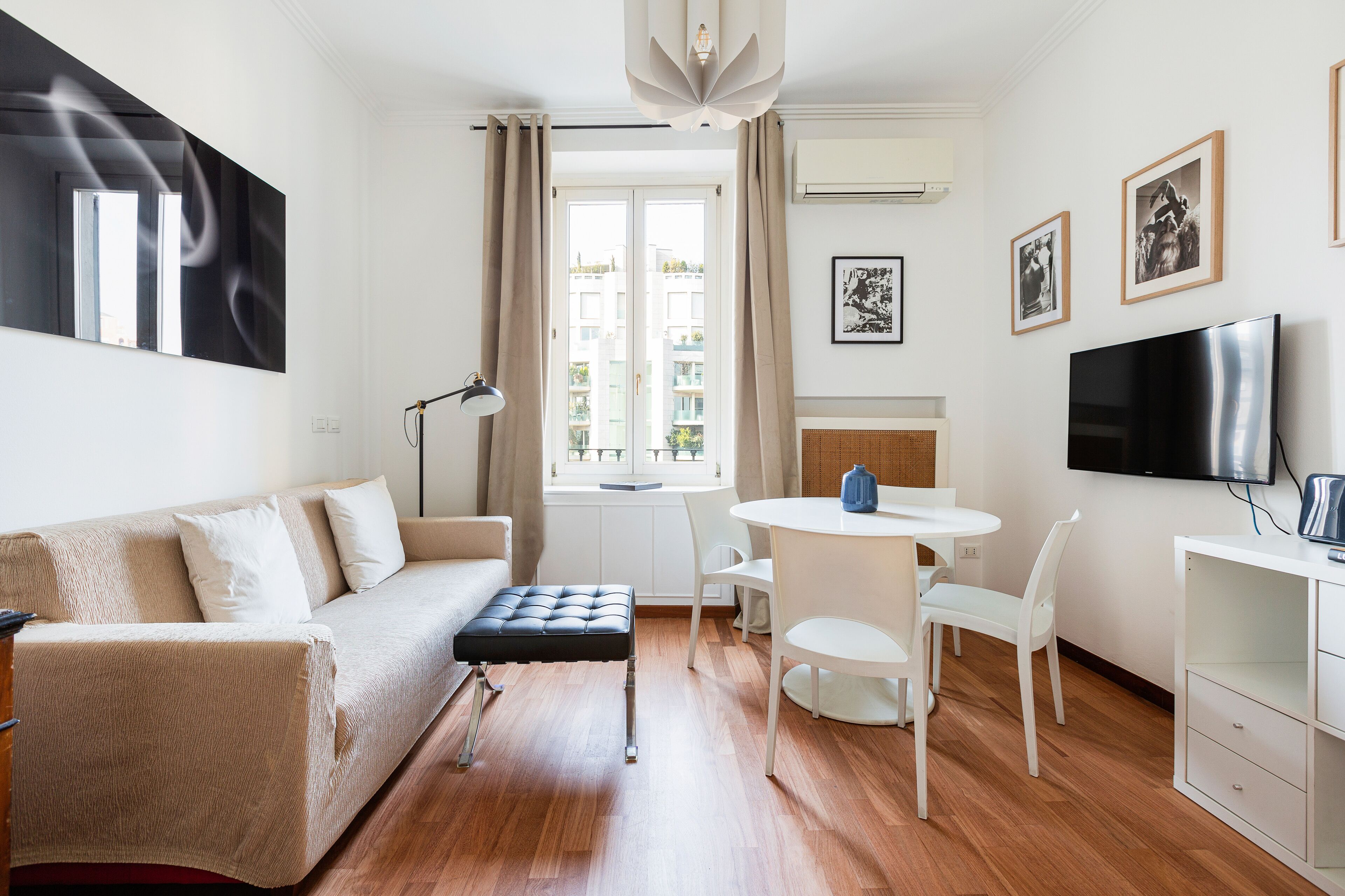 A modern living room with a sofa, ottoman, dining table, chairs, and a TV.