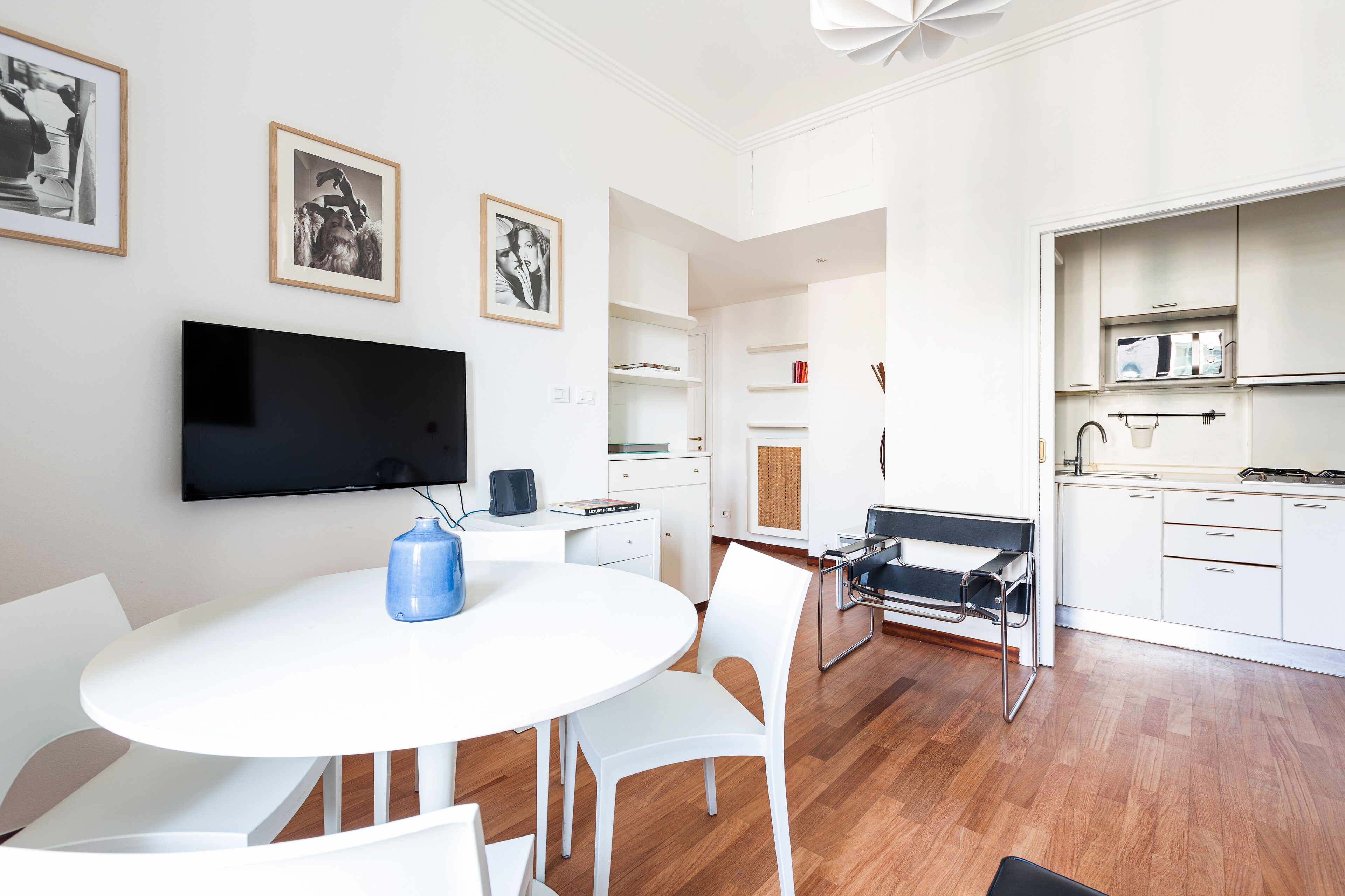 A modern, open-plan living space with a dining area, kitchen, and a flat-screen TV mounted on the wall.