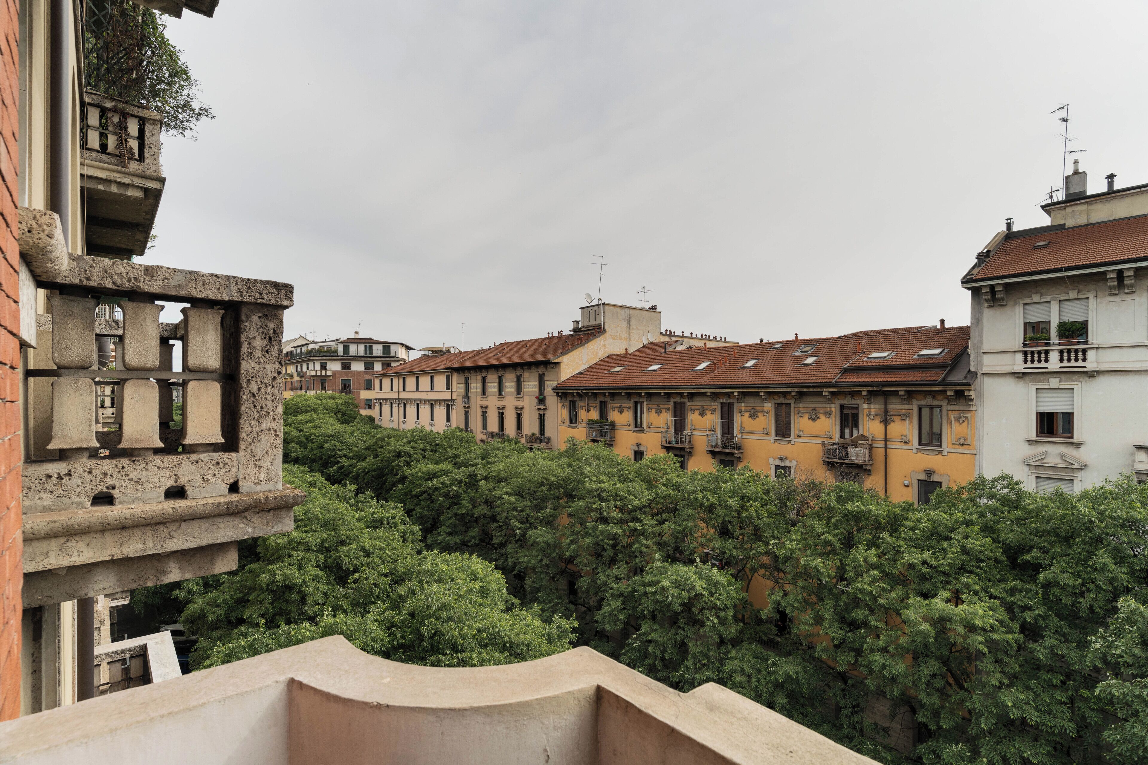A courtyard with buildings, trees, and a stone balustrade.