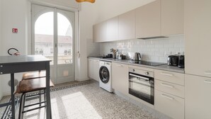 A compact kitchen with a washing machine, oven, and a dining area with a table and chairs. - Brera Apartments in Porta Venezia (Milan)