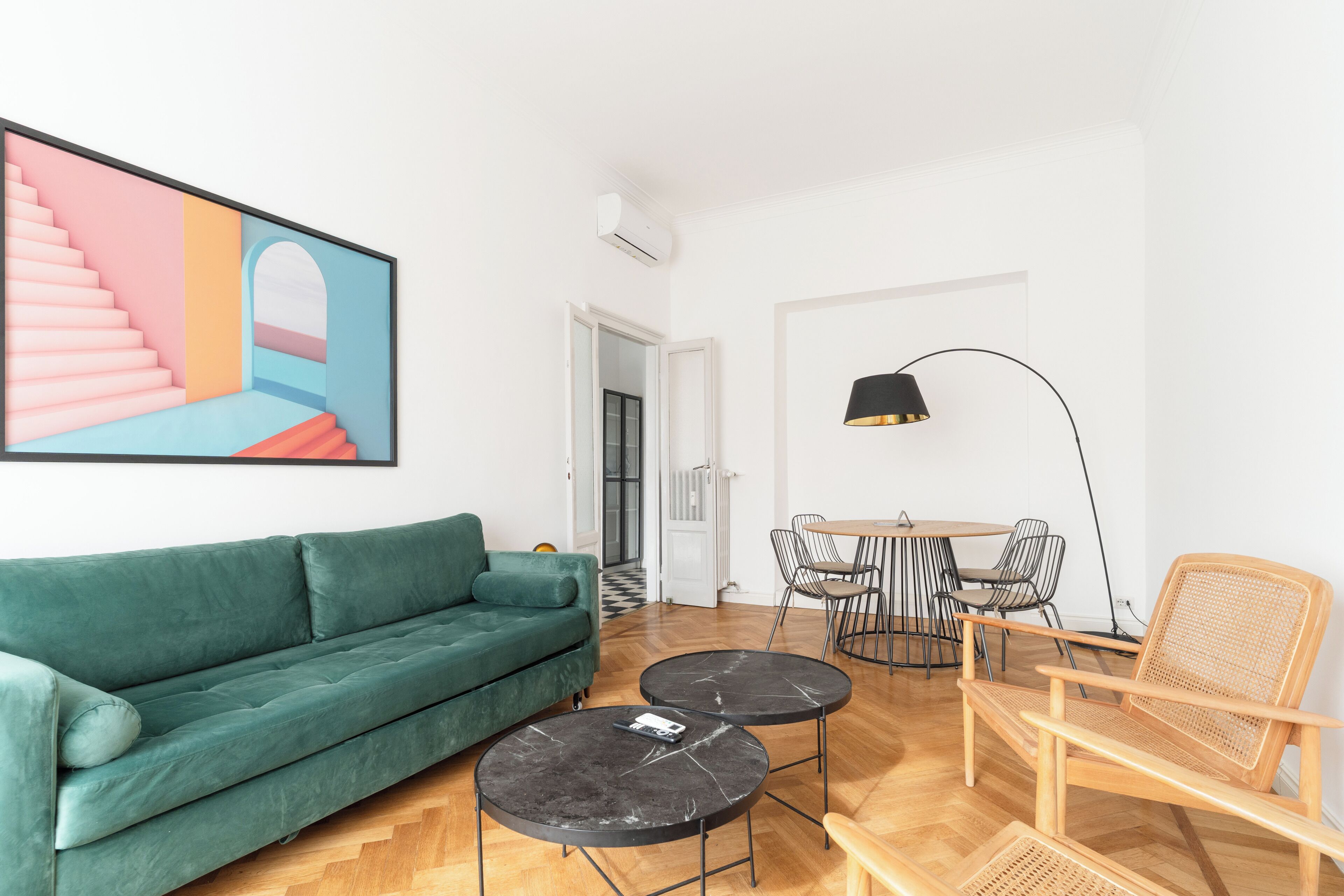A living room with a green sofa, two round tables, a chair, and a painting on the wall.
