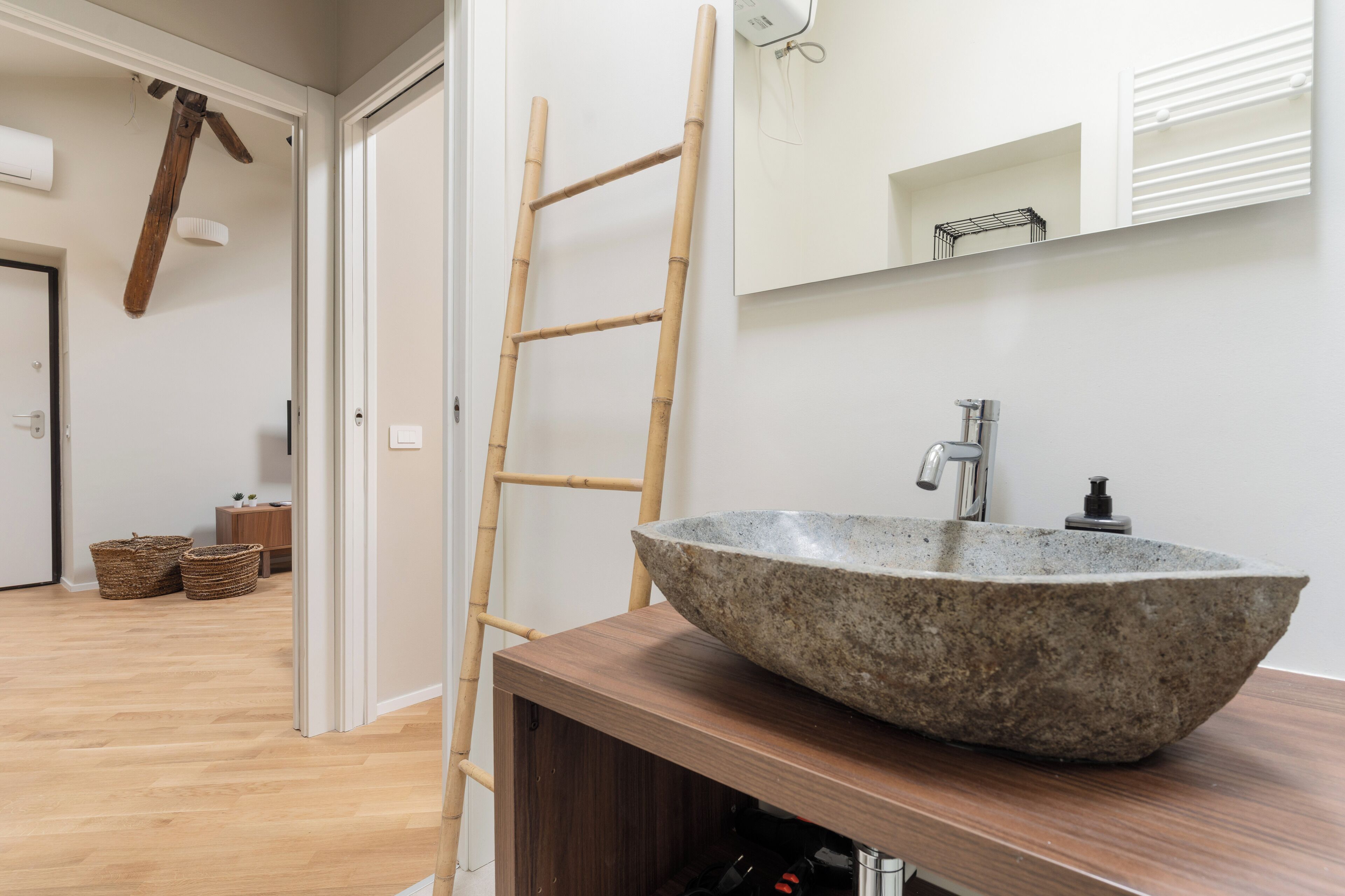 A bathroom with a large stone sink, a wooden ladder, and a mirror above the sink.