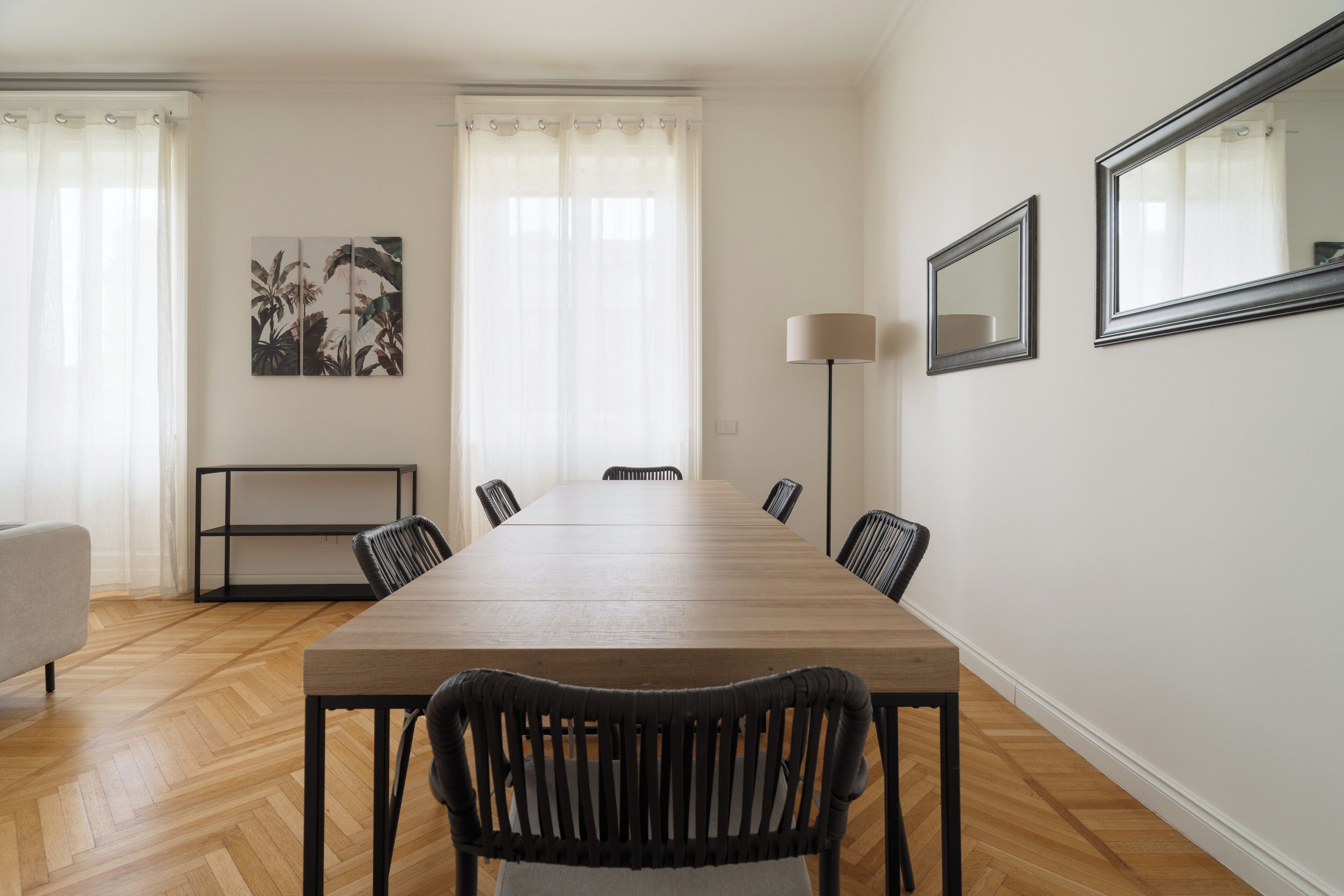 A dining area with a long wooden table, black chairs, a sofa, and a lamp.