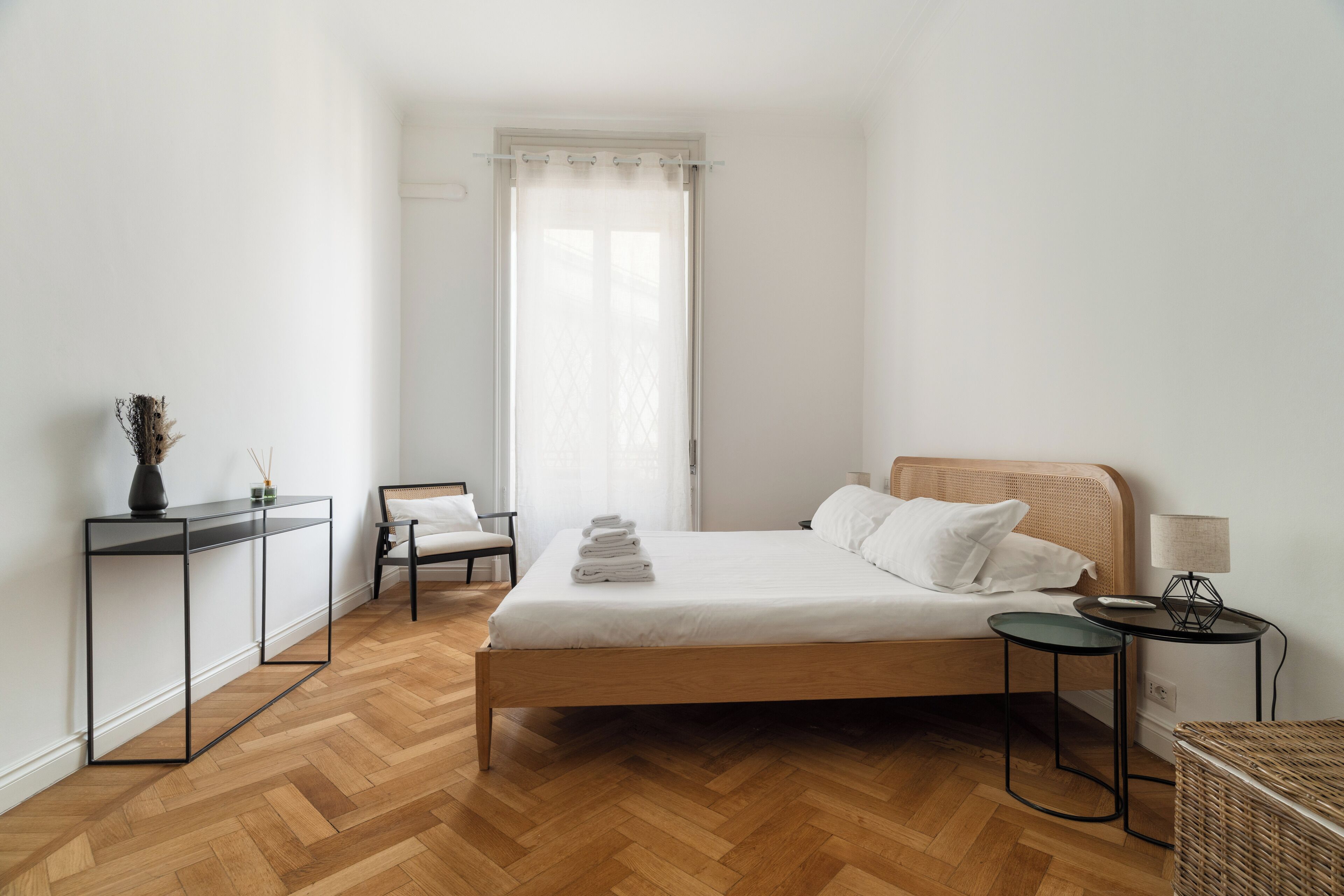 Une chambre à coucher avec un lit, des tables de chevet, une chaise, une petite table et une fenêtre avec des rideaux.