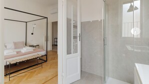 A bedroom with a four-poster bed, a glass shower enclosure, and a hallway leading to another room. - Brera Apartments in Porta Venezia (Milan)