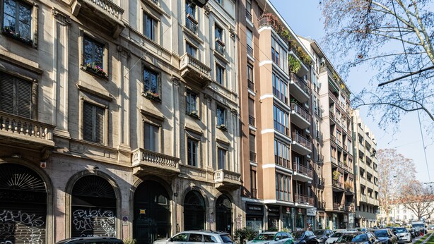 A multi-story building with balconies, arched windows, and a variety of shops on the ground floor. - Brera Apartments in Porta Venezia (Milan)