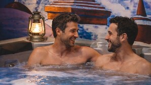Dos hombres en un jacuzzi con un mural de una escena nevada de montaña al fondo.