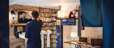 Un baño con espejo, lavamanos y una estantería llena de libros.