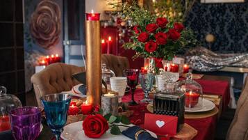 Un ambiente romántico para cenar, con un centro de mesa de velas, rosas rojas y una tarjeta con forma de corazón sobre la mesa.