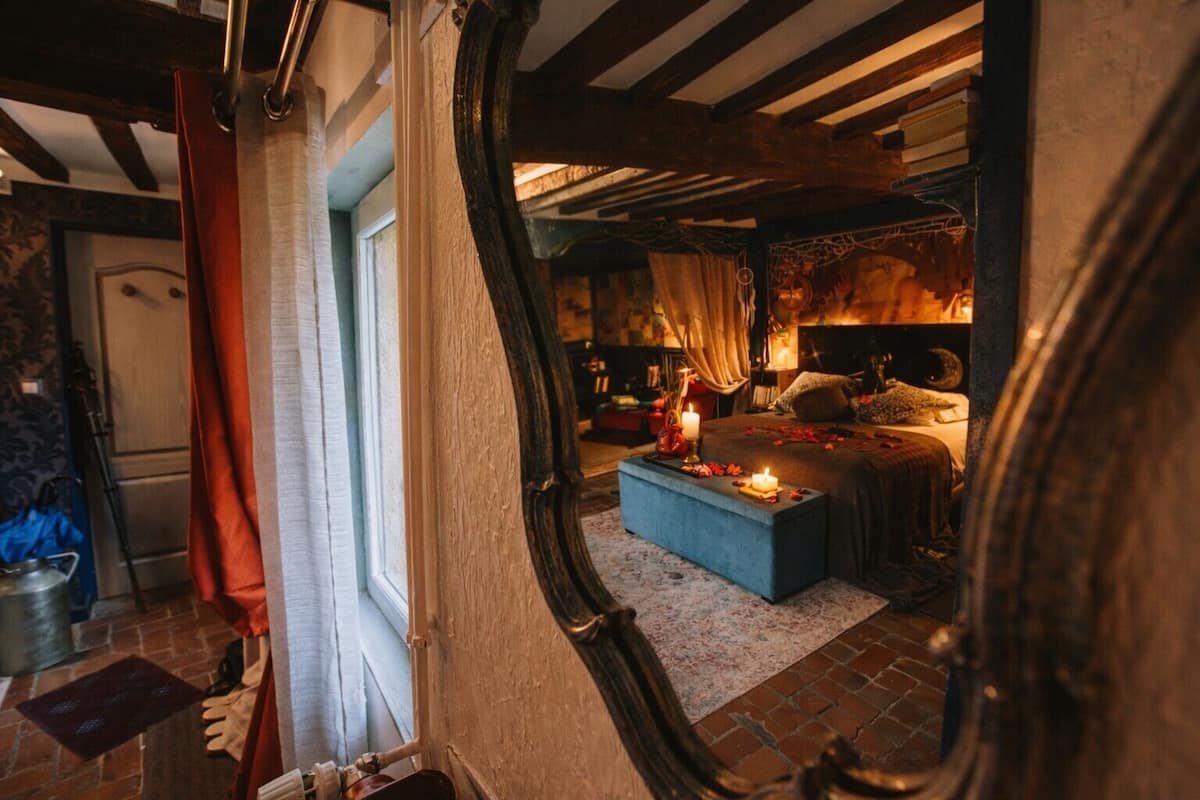 Um quarto acolhedor com uma cama grande, uma mesa de cabeceira com velas e um espelho refletindo o aposento.