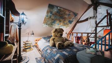 Acogedor dormitorio en ático con un gran oso de peluche sobre la cama, una escalera de madera y un cuadro abstracto colgado.