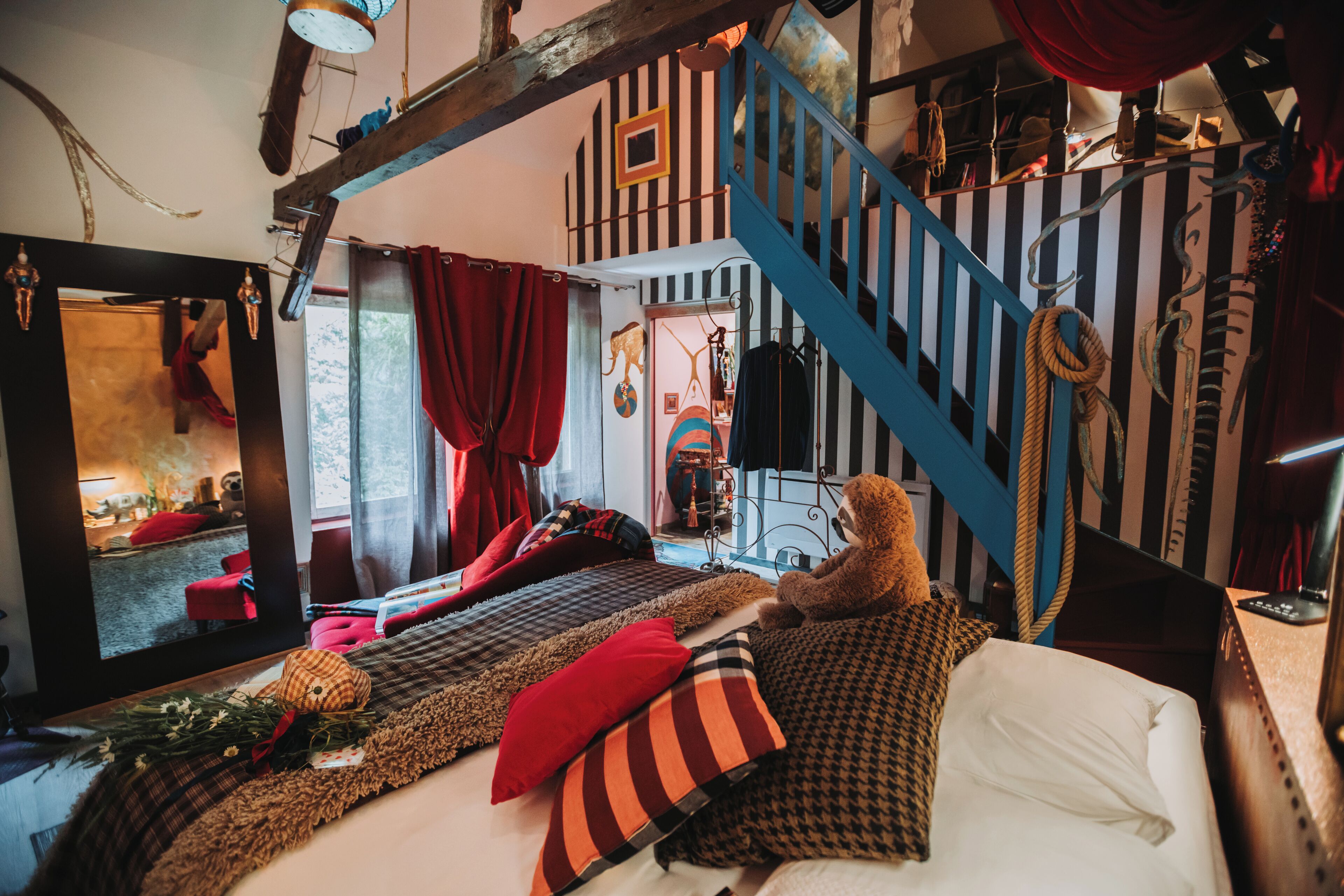 A cozy bedroom with a bed, pillows, a teddy bear, a mirror, and a staircase.