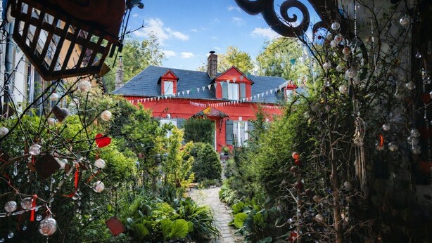 Una casa roja con un sendero de piedra que la conduce, rodeada de abundante vegetación y elementos decorativos.