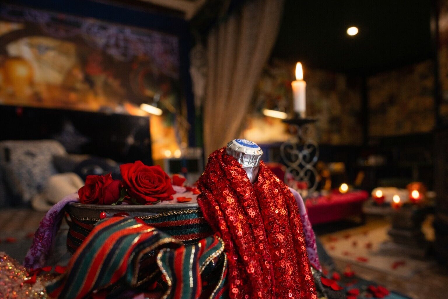 Une chambre avec un lit, une table décorative ornée d’une rose rouge et une bougie.