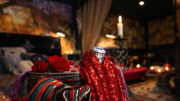 Une chambre avec un lit, une table décorative ornée d’une rose rouge et une bougie.