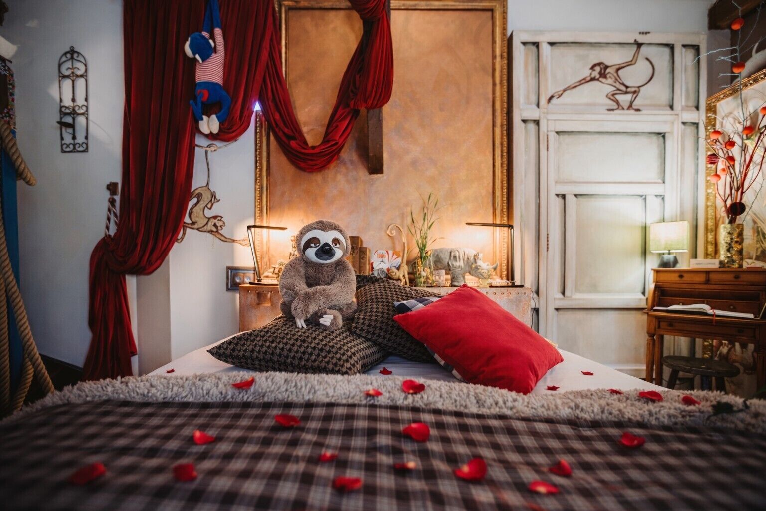 A cozy bedroom with a plush bed, a sloth plush toy, red curtains, and a vintage lamp.