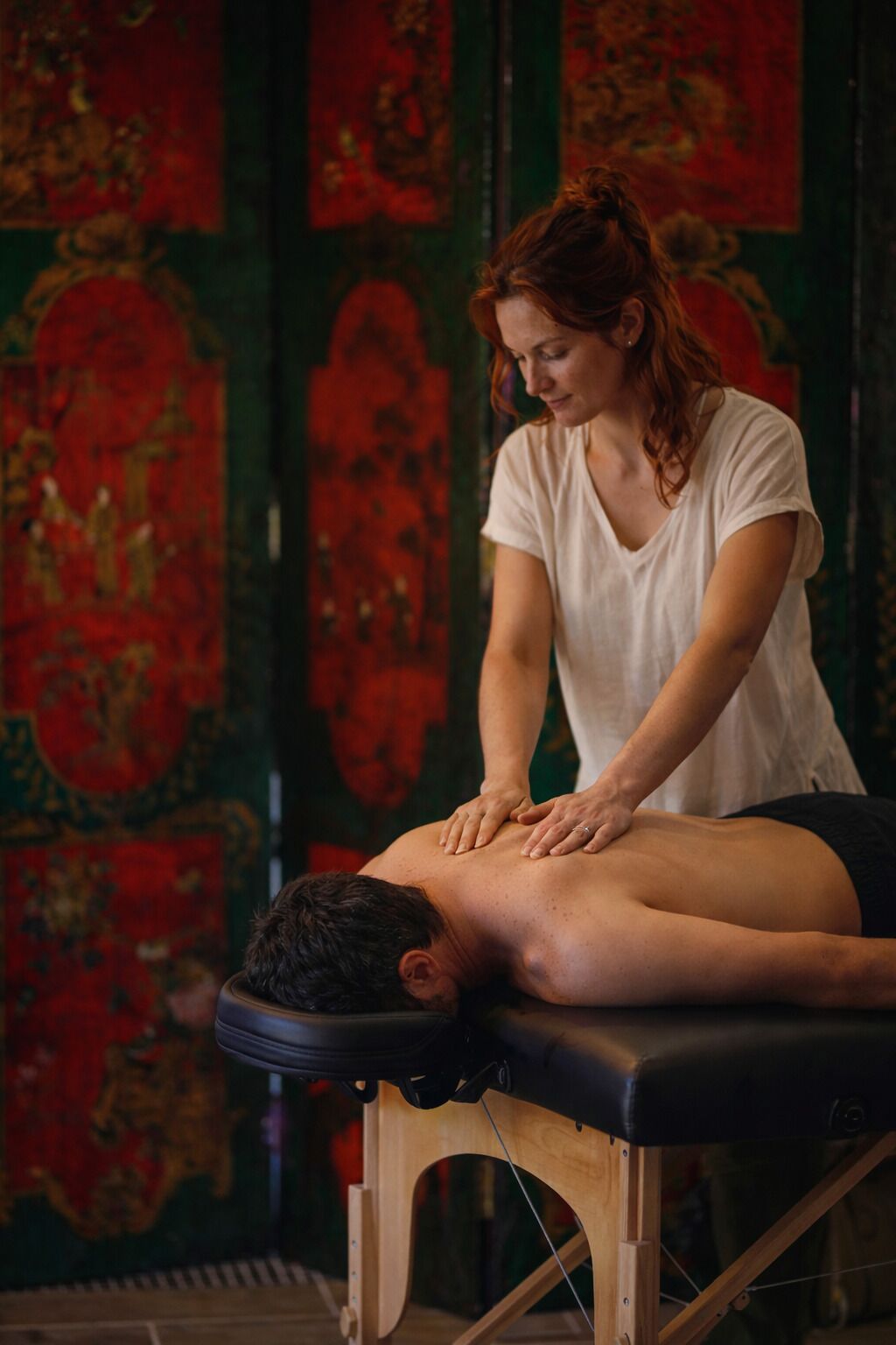 Une séance de massage dans une pièce où se trouve une table de massage en bois, et où une personne reçoit un massage du dos.
