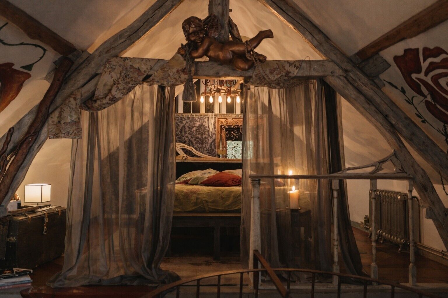 A cozy attic bedroom with a sloped ceiling, a bed with a floral bedspread, a nightstand with a lamp, and a decorative angel sculpture.