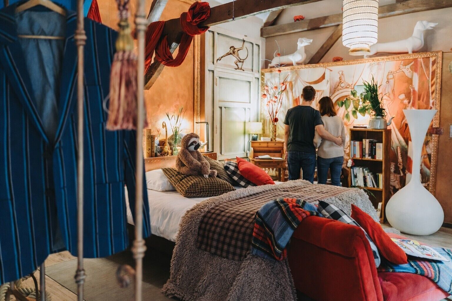 A cozy bedroom with a large bed, a sloth plush toy, and a bookshelf filled with books.