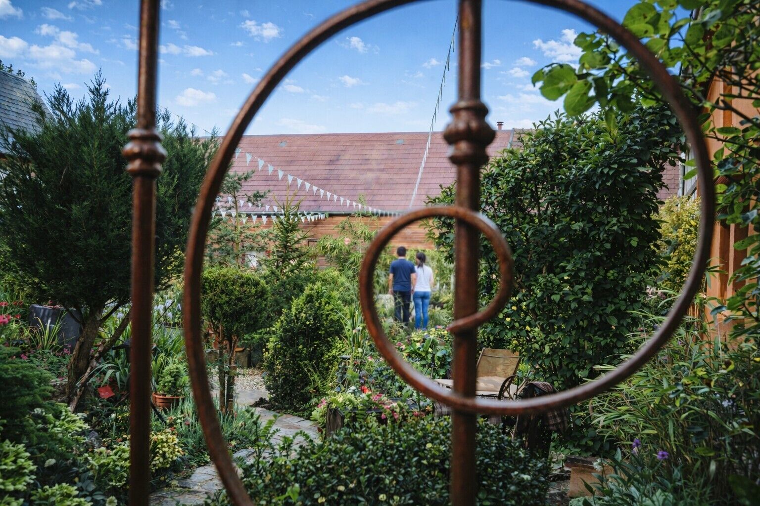 Un jardín con una valla de metal, un sendero y un edificio al fondo.
