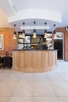 Uma área de bar moderna com balcão de madeira, iluminação pendente e parede de tijolos ao fundo.