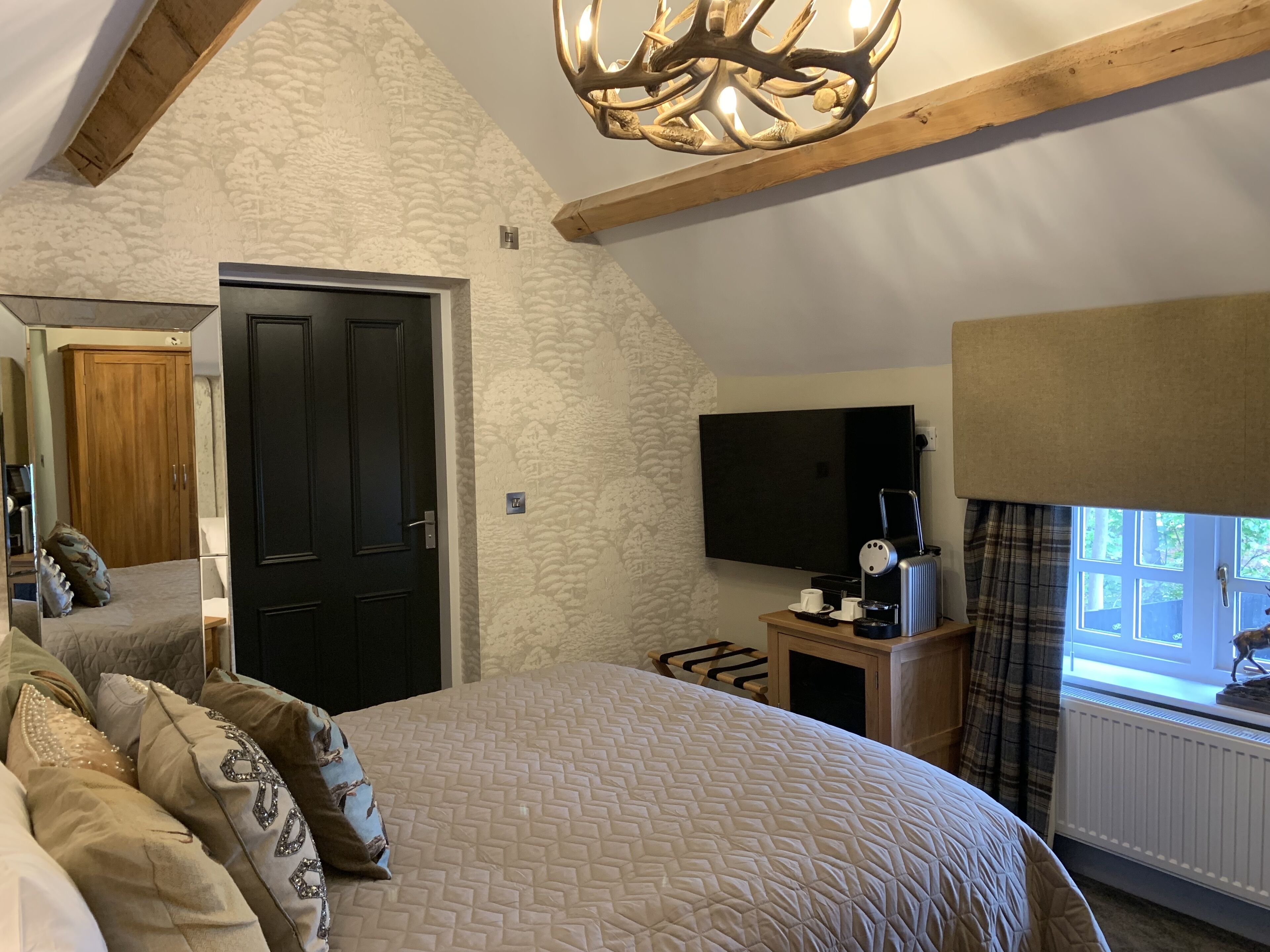 A bedroom with a bed, a television, a window with curtains, and a wooden ceiling.
