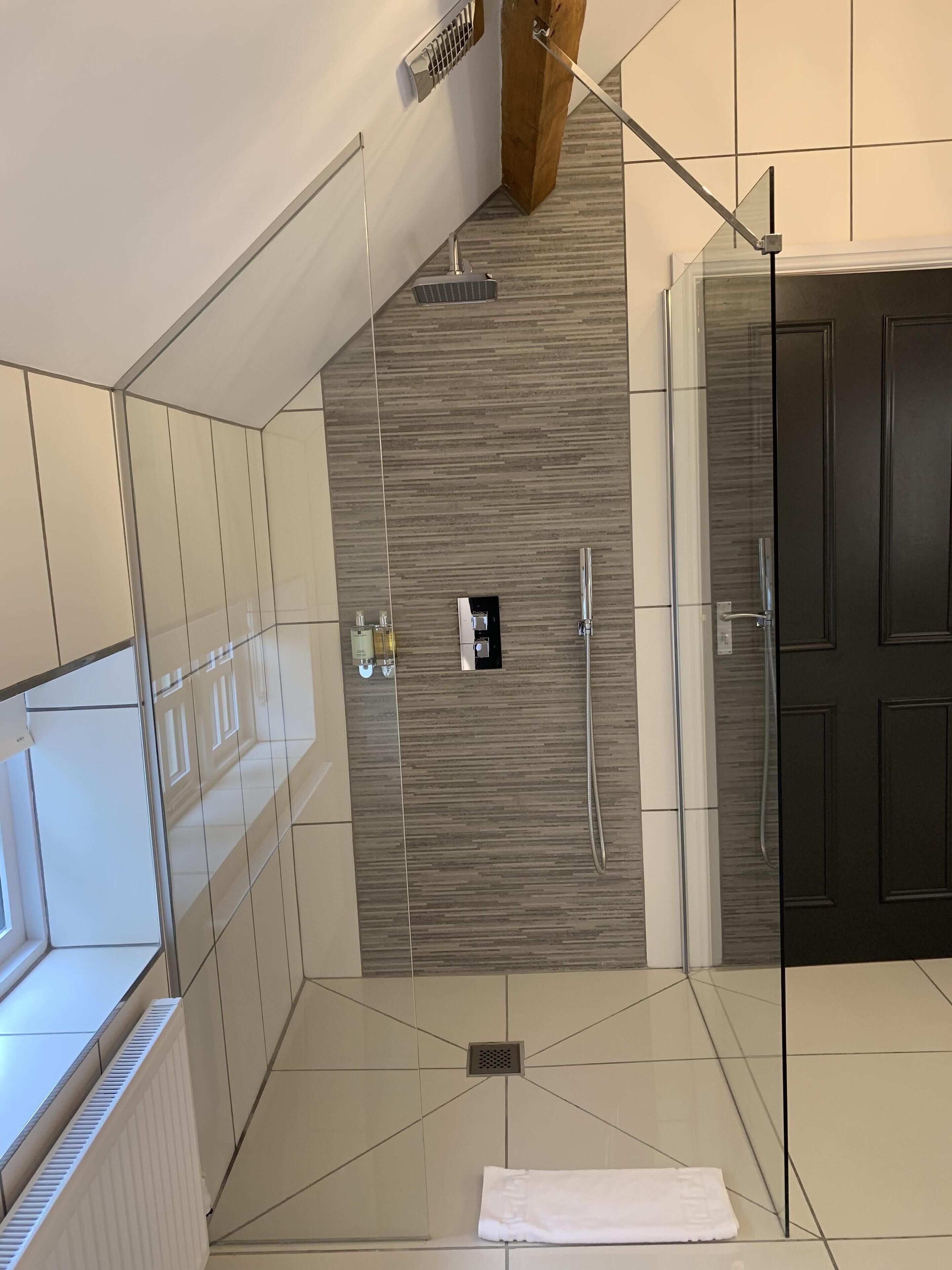 A modern bathroom with a glass shower enclosure, a towel rack, and a dark wooden door.
