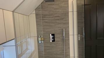 A modern bathroom with a glass shower enclosure, a towel rack, and a dark wooden door.